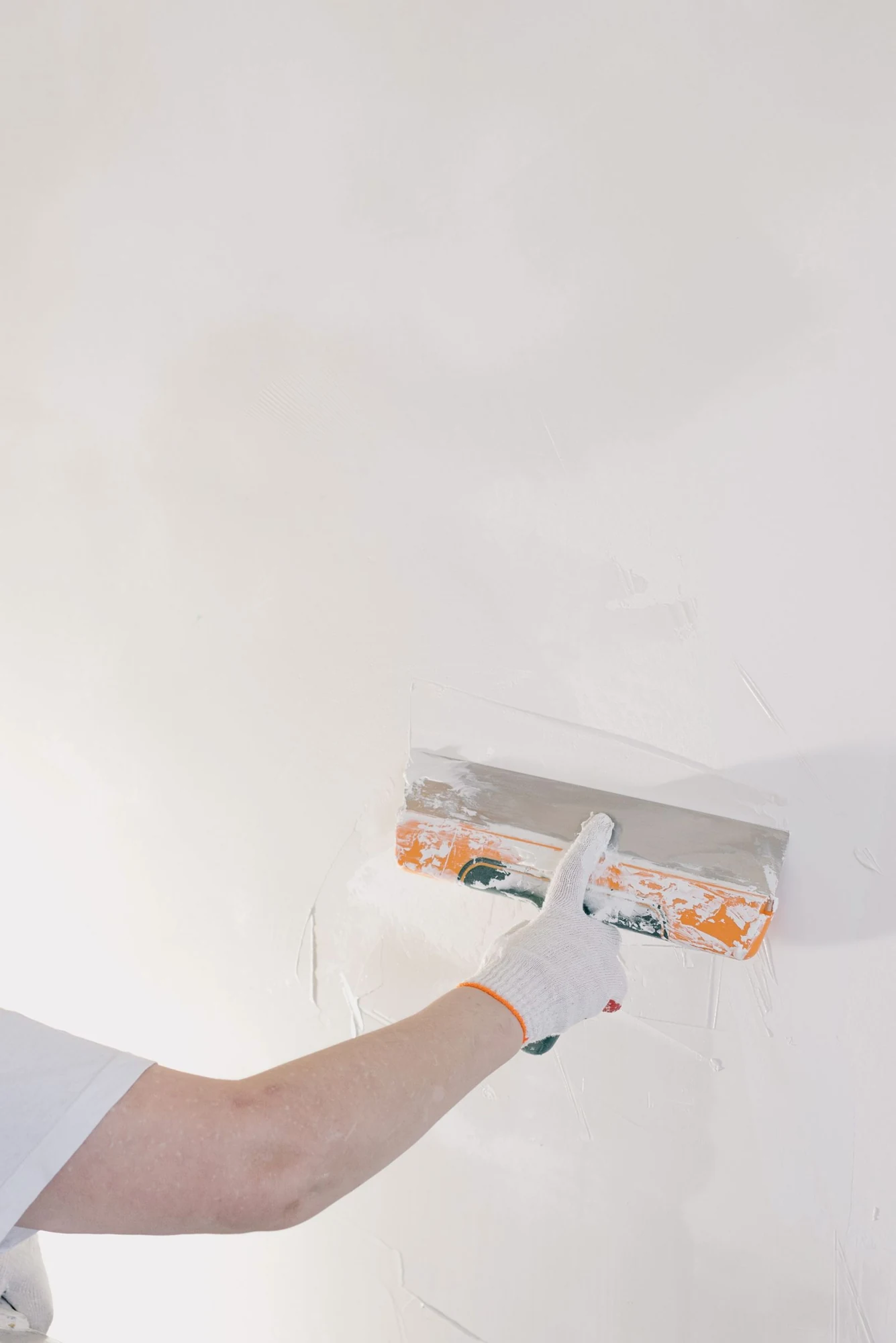 Een gehandschoende hand verdeelt pleister over een lichte wand.