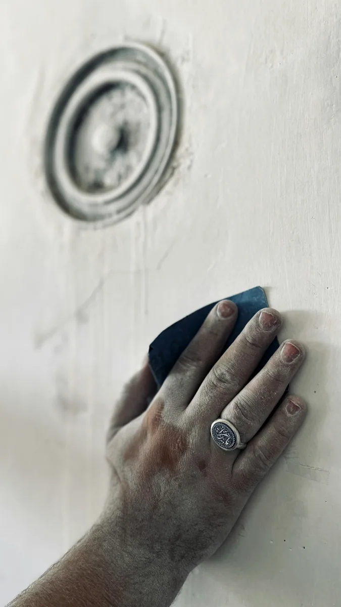 Een hand bewerkt een wandoppervlak met schuurmateriaal. — illustratieve foto