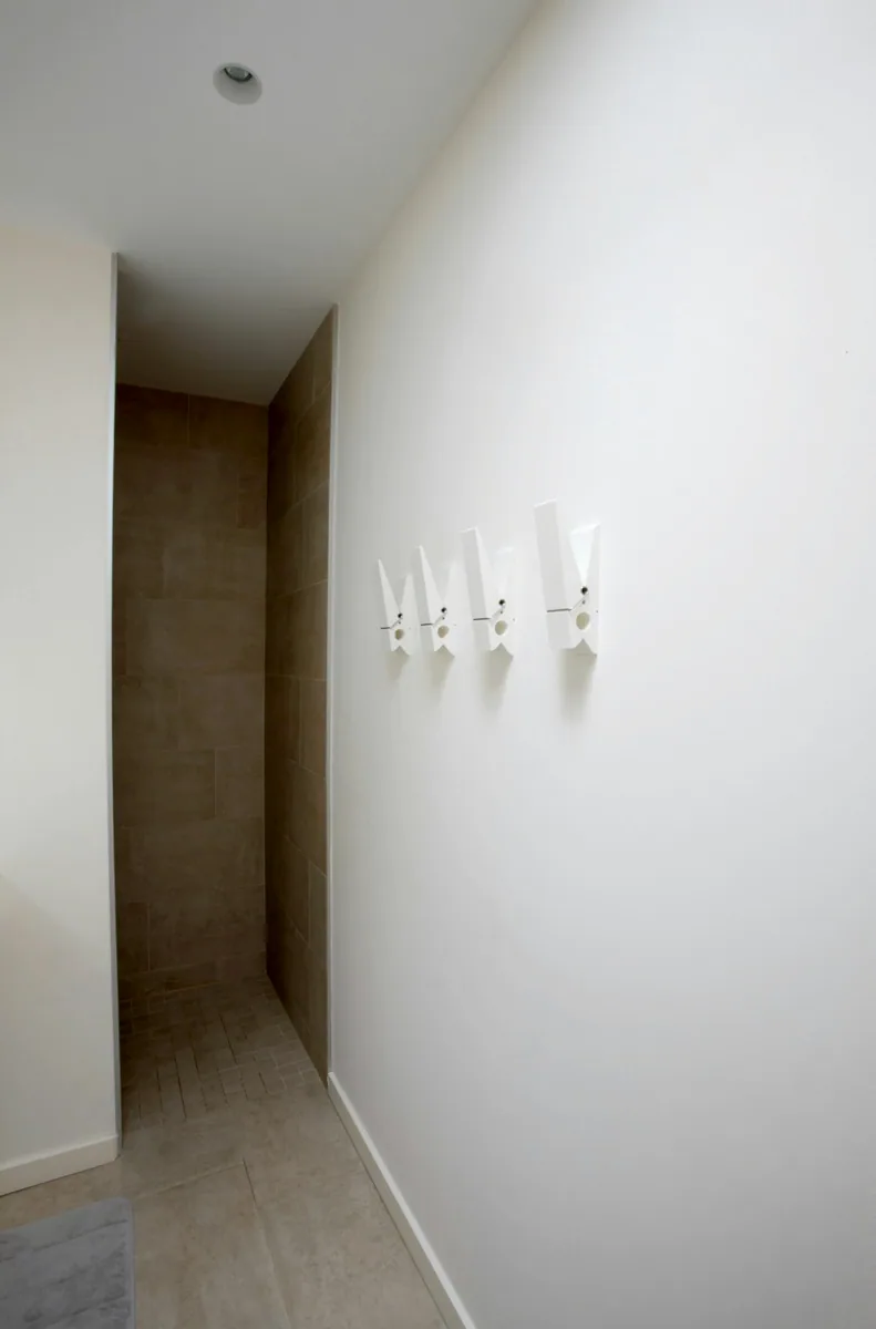Een witte halwand met eenvoudige kapstokhaken. — illustratieve foto